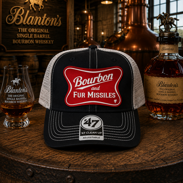 Trucker hat with 'Bourbon for Missiles' design on a wooden barrel with Blanton's whiskey bottles and glasses.